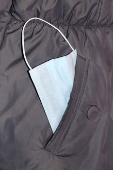 medical mask in the pocket of a gray jacket close-up