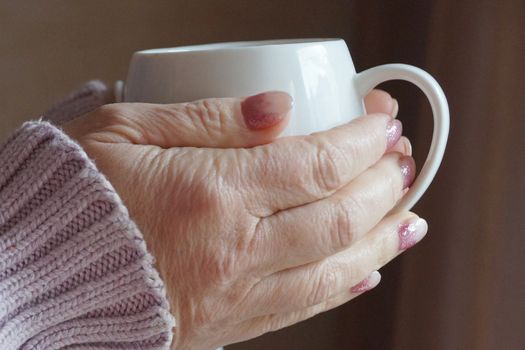 female hands in a warm sweater hold a hot cup