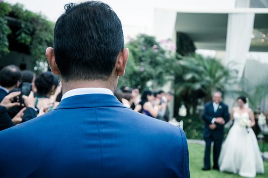 Outdoor Groom is waiting for bride who is coming with her dad in the wedding