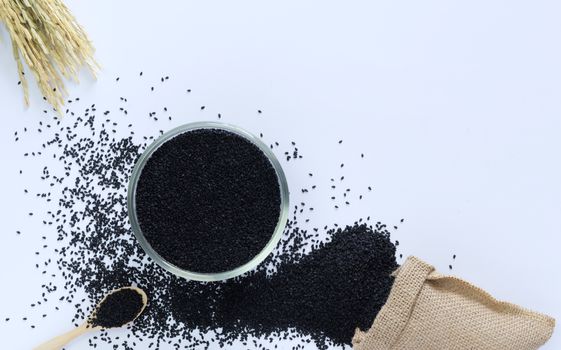 Black sesame in a cup on a white background with wooden spoon, sacks and ears of rice are elements.