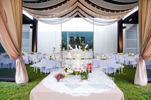 A wide angle view of a wedding reception venue, with dance floor and surrounding tables. A large chandelier in the middle of the room has tooling draped from it, with mini lights.