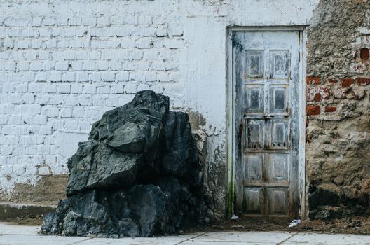 Old door of a house on the edge of the white beach with a large rock next to it, located on San Bartolo beach, Lima - Peru