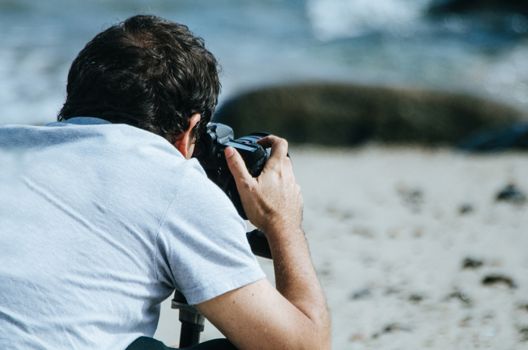 Traveling and photography. Young man with camera taking picture on the sea beach.
