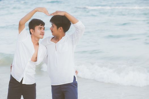 Homosexual portrait young asian couple stand gesture heart shape together on beach in summer, asia gay hug and going sea for leisure with romantic and happy in vacation, LGBT with legal concept.