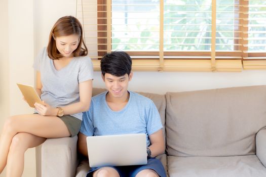 Beautiful young asian couple cheerful freelance working with man using laptop and woman using tablet on couch, family relax and sharing communication together at home, lifestyle concept.