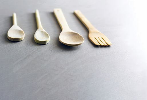 Group of wooden kitchen utensils arranged on a gray marble table. Selective focus on the carving fork.