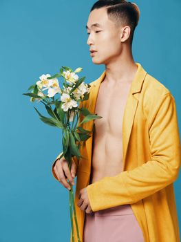 A young man of Asian appearance with a bouquet of flowers looks to the side on a blue background. High quality photo