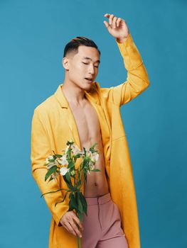 Side view of a handsome man with a bouquet of white flowers and in pink trousers gesturing with his hands on a blue background. High quality photo