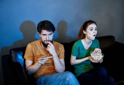 A woman and a man with popcorn on a leather sofa indoors watching TV in the evening. High quality photo