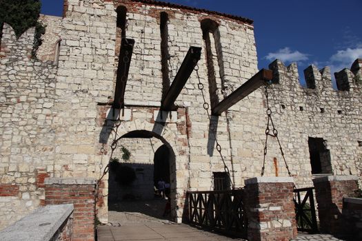 Stone wall with merlons and drawbridge gate of medieval castle of Brescia in north Italy