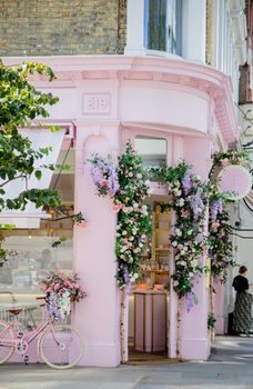 London, UK - September 30, 2020: Portrait View of a Pink Cake Shop Entrance surrounded by flowers,and with a pink Bicycle Outside