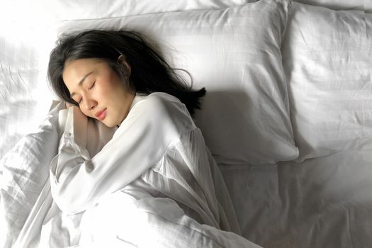 Beautiful Asian woman sleeping in bed under white quilt with head on pillow comfortable and happy. girl with relax for health concept.