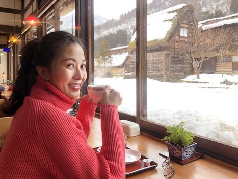 Woman tourist drinking coffee in the morning  and enjoying the winter snow view at Shirakawago village, Gifu, Japan.