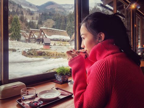 Woman tourist drinking coffee in the morning  and enjoying the winter snow view at Shirakawago village, Gifu, Japan.