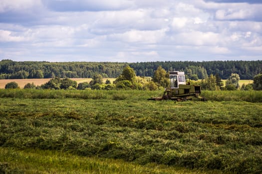 TULA, RUSSIA - JULY 30, 2019: green haymaking tractor on summer field before storm - telephoto shot with selective focus and blur.