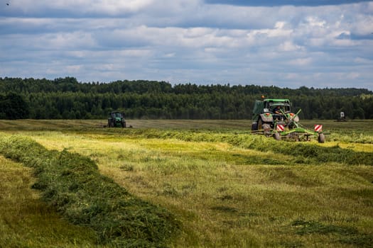 TULA, RUSSIA - JULY 30, 2019: green haymaking tractor on summer field before storm - telephoto shot with selective focus and blur.