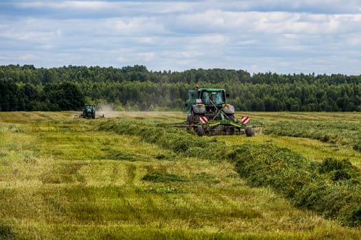 TULA, RUSSIA - JULY 30, 2019: green haymaking tractor on summer field before storm - telephoto shot with selective focus and blur.