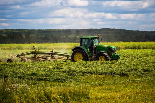 TULA, RUSSIA - JULY 30, 2019: green haymaking tractor on summer field before storm - telephoto shot with selective focus and blur.