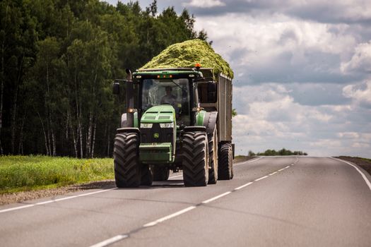 TULA, RUSSIA - JULY 30, 2019: tractor with green ensilage in the trailer rolling on summer road.
