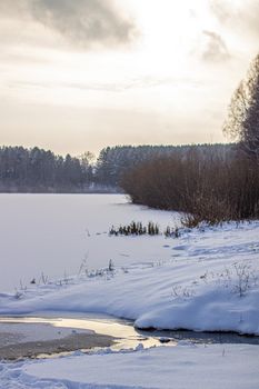 Dramatic sky with clouds over the winter forest and lake. Winter and frosty nature. Frozen lake near the forest, all covered in snow.