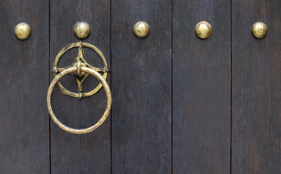 Shining solid brass metal round door knocker on old dark wooden door.