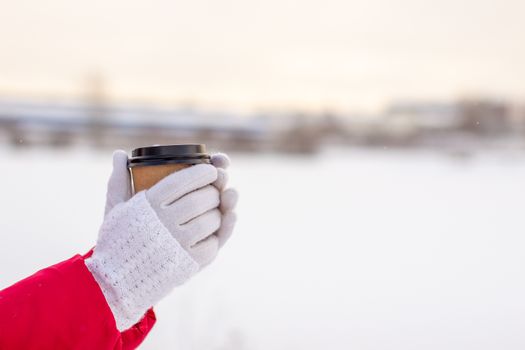 A young woman in a red jacket in winter holds a glass of hot coffee or tea. A snowy winter and a hot drink to keep you warm. A glass of coffee in winter.