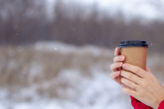 A young woman in a red jacket in winter holds a glass of hot coffee or tea. A snowy winter and a hot drink to keep you warm. A glass of coffee in winter.
