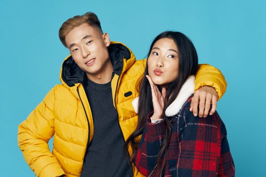 Fashionable young couple of Asian appearance in winter clothes hugs studio blue background