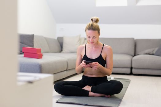 Beautiful blonde woman doing home workout indoors. Woman practice yoga at home. Fit girl using workout tutorials for healthy active lifestyle. Woman using quarantine for home workouts. Stretching