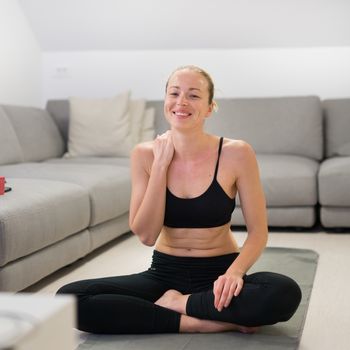 Beautiful blonde woman doing home workout indoors. Woman practice yoga at home. Fit girl using workout tutorials for healthy active lifestyle. Woman using quarantine for home workouts. Stretching