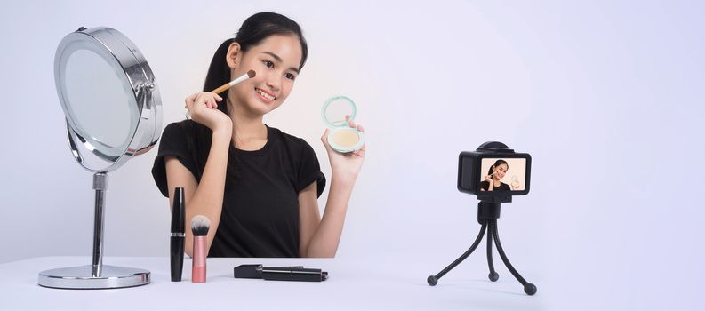 Asian teen woman sit in front of camera and live broadcasting as a beauty blogger influencer or youtuber to review or advice about how to make up at home. studio shot white background.