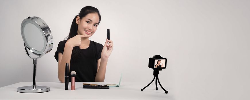 Asian teen woman sit in front of camera and live broadcasting as a beauty blogger influencer or youtuber to review or advice about how to make up at home. studio shot white background.