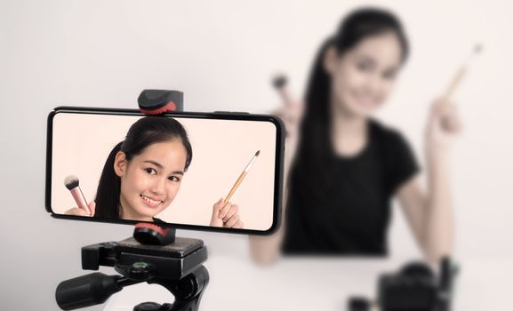 Asian teen woman sit in front of camera and live broadcasting as a beauty blogger influencer or youtuber to review or advice about how to make up at home. studio shot white background.