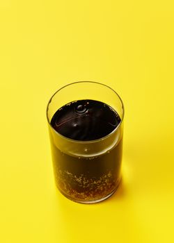 Glass with cola on yellow table, close up detail.