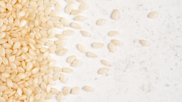 White sesame - Sesamum indicum - seeds on white stone like board, view from above.