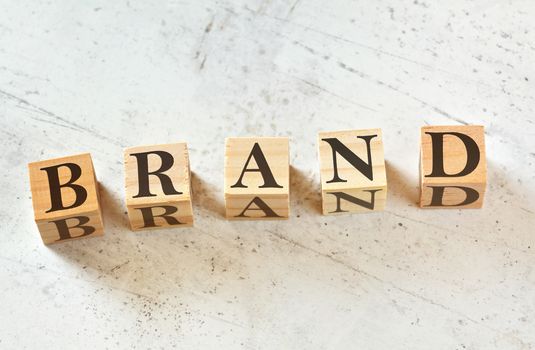 Five wooden cubes with word BRAND on white stone like board, view from above.