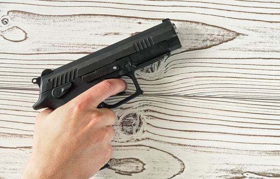 Man hand holding black modern metal gun on white wooden table, closeup detail.