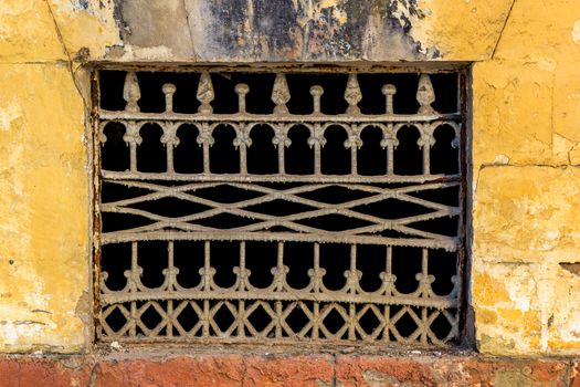 Old yellow wall with closed window with old painted iron grid front