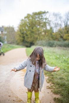 Little girl looking adorably at her muddy clothes after jumping in puddle. Young child having fun and getting dirty in puddles. Kids playing outside