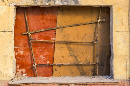 Old yellow wall with closed window with old rusty iron grid front