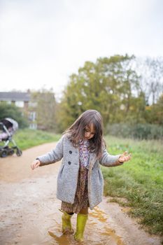 Happy little girl calmly splashing and walking through a muddy puddle. Young child having fun and getting dirty in puddles. Kids playing outside