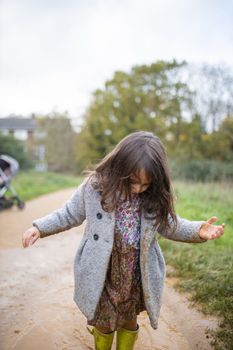 Little girl looking down at her muddy clothes after jumping in puddle. Young child having fun and getting dirty in puddles. Kids playing outside