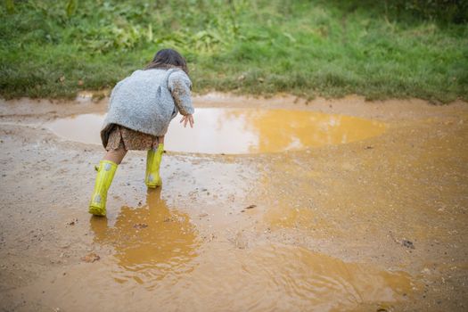Happy little girl on dirt road taking momentum before jumping in a muddy puddle. Young child having fun jumping in puddles. Kids playing outside