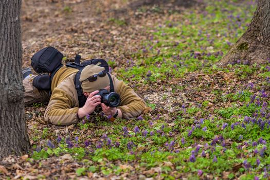 Professional photographer laying on ground and shooting hidden. Selective focus technique with background blur.