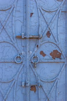 Old forged iron door with rivets and old peeling blue paint on it