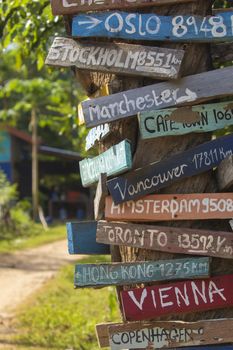 Colourful hand painted direction wood signs to different cities of the world, and mileage marker in Don Det island, one of the famous Four Thousand Islands or Si Phan Don, in the Mekong river, Laos.