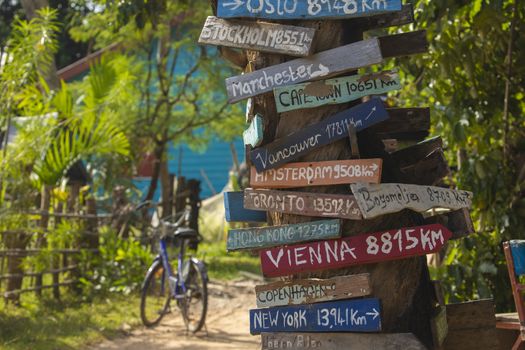 Colourful hand painted direction wood signs to different cities of the world, and mileage marker in Don Det island, one of the famous Four Thousand Islands or Si Phan Don, in the Mekong river, Laos.