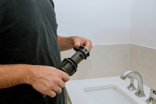 Hand plumber holds sewer drain an assembly near the faucet