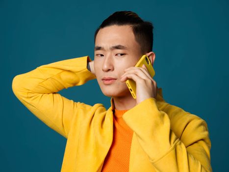 Man talking on the phone narrow eyes yellow jacket blue background. High quality photo