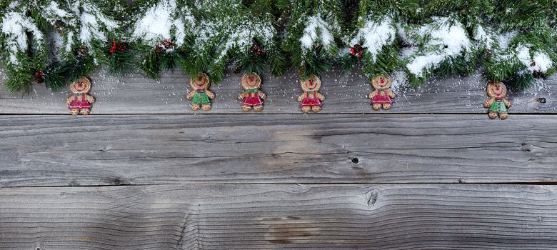 Christmas rustic natural wooden background with snow covered evergreen branches and Gingerbread cookie figures  